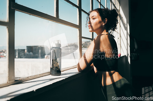 Image of Window, fitness and relax with a sports woman looking at the view during a break in the gym for exercise. Health, wellness and training with a female athlete taking a break from her studio workout