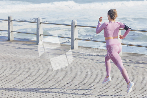 Image of Woman, fitness and running by sea, outdoor and fast for wellness, health and goals in summer. Runner girl, speed and balance in sunshine with smartphone, wearable tech and waves by ocean in Cape Town