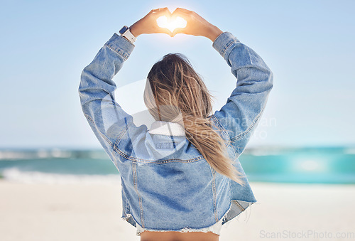 Image of Heart, hands and back view of woman at beach love, care and kindness, trust and support. Girl, sea and finger shape for wellness, nature and peace for earth day, blue sky and ocean travel in sunshine