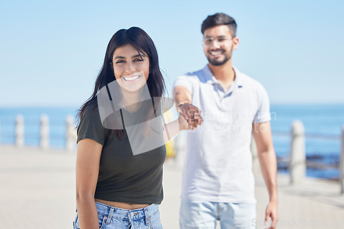 Image of Beach, love and portrait of a happy couple holding hands while on a seaside summer vacation. Happiness, smile and young man and woman from India walking on the promenade by the ocean while on holiday