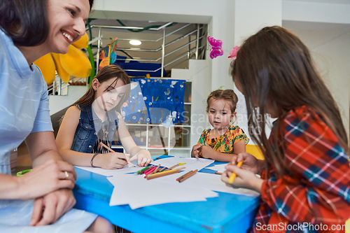 Image of Creative kids during an art class in a daycare center or elementary school classroom drawing with female teacher.