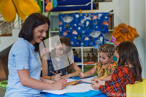 Image of Creative kids during an art class in a daycare center or elementary school classroom drawing with female teacher.