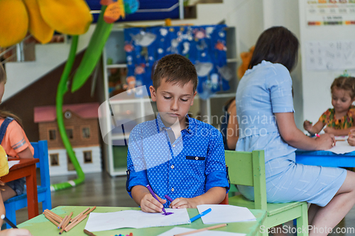 Image of Creative kids during an art class in a daycare center or elementary school classroom drawing with female teacher.