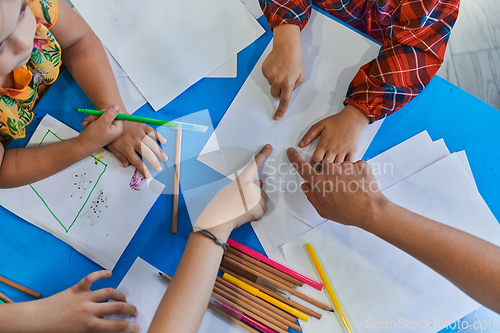 Image of Creative kids during an art class in a daycare center or elementary school classroom drawing with female teacher.