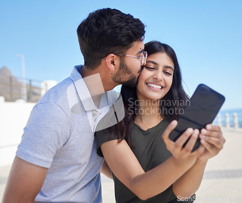 Image of Phone, selfie and smile with couple at beach, travel and kiss by ocean with support, trust and outdoor for adventure in Mumbai. Smile in picture, happy memory with smartphone photography and romance