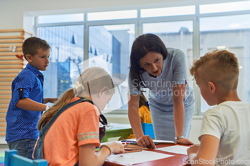 Image of Creative kids during an art class in a daycare center or elementary school classroom drawing with female teacher.