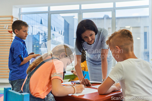 Image of Creative kids during an art class in a daycare center or elementary school classroom drawing with female teacher.