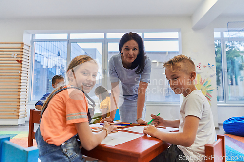 Image of Creative kids during an art class in a daycare center or elementary school classroom drawing with female teacher.