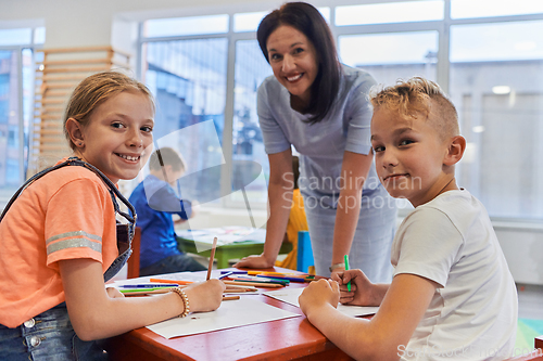 Image of Creative kids during an art class in a daycare center or elementary school classroom drawing with female teacher.