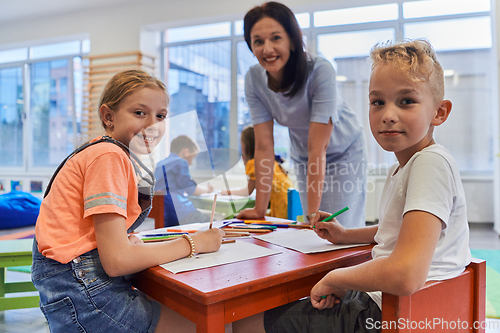 Image of Creative kids during an art class in a daycare center or elementary school classroom drawing with female teacher.