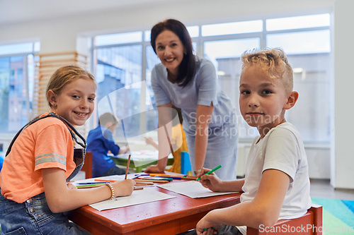 Image of Creative kids during an art class in a daycare center or elementary school classroom drawing with female teacher.