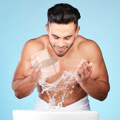 Image of Face, water splash and skincare of man cleaning in studio isolated on a blue background. Hygiene, water drops and male model washing, bathing or grooming for healthy skin, facial wellness or beauty.