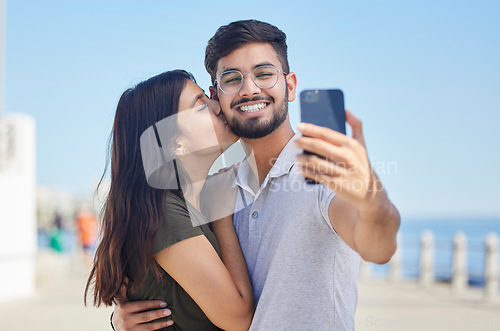 Image of Phone, kiss or couple love taking a selfie on a romantic honeymoon, beach holiday or vacation in a summer romance. Smile, profile pictures or happy man enjoys quality bonding time with Indian partner