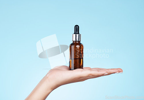 Image of Hand, product and serum with a woman in studio on a blue background to promote an antiaging treatment. Skincare, beauty and bottle with a female model holding a container for cosmetic advertising