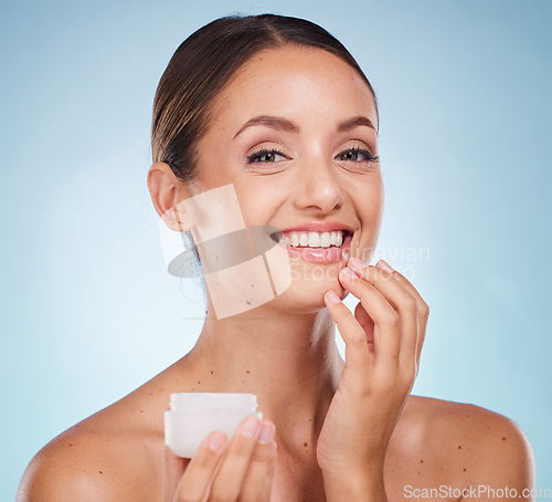 Image of Portrait, skincare or lotion with a model woman holding a container in studio on blue background to promote beauty. Face, wellness or luxury and an attractive young female with cream to apply on skin