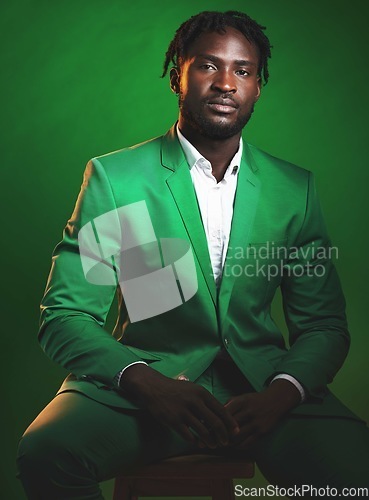 Image of Fashion, formal and black man in a green suit sitting on a chair in studio with a luxury outfit. Elegant, stylish and portrait of an African male model with fashionable clothes isolated by background