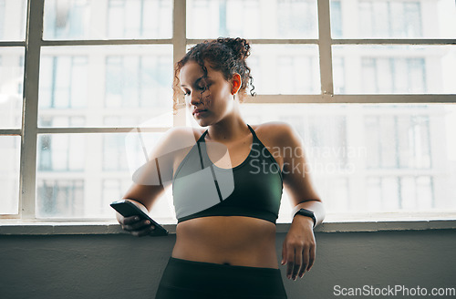 Image of Idea, phone and exercise with a sports woman by a window, standing in the gym during a fitnesss workout. Health, thinking and a female athlete using social media or an app to track her training