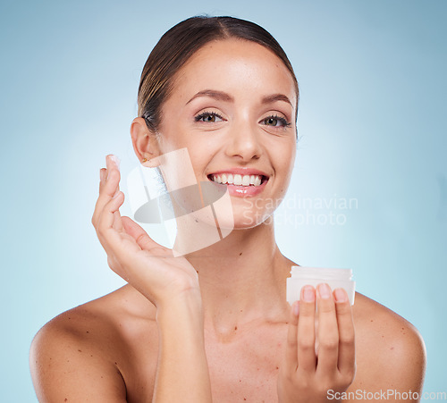 Image of Portrait, beauty and skincare product with a model woman holding a container in studio on a blue background. Face, wellness or luxury and an attractive young female with cream to apply on skin