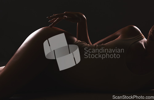 Image of Lingerie, shadow and silhouette of sexy woman relax in erotic, sexual and seductive underwear on dark black background. Sexuality, creativity and body of aesthetic model girl with creative beauty