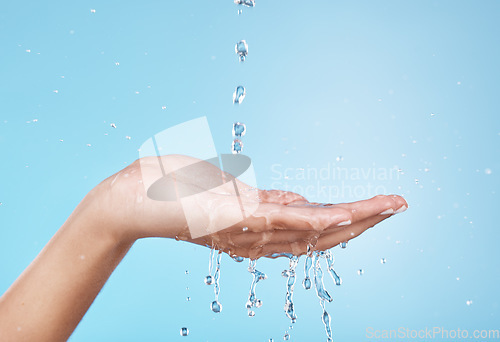 Image of Hand, water and hydration with a woman cleaning in studio on a blue background for hygiene or personal care. Water splash, health and skincare with a female washing hands in the shower or bathroom