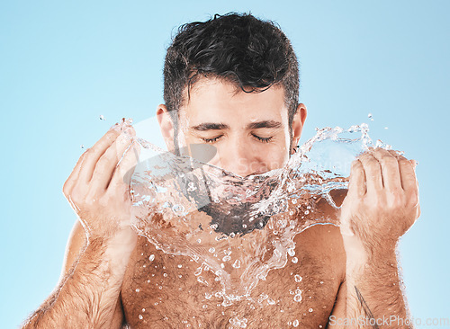 Image of Man, splash and face for beauty in studio for wellness, health or self care cleaning by blue background. Model, bathroom and water drops with hands for healthy facial, self love and cosmetic backdrop