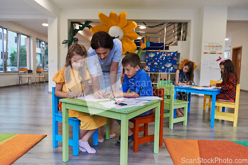 Image of Creative kids during an art class in a daycare center or elementary school classroom drawing with female teacher.