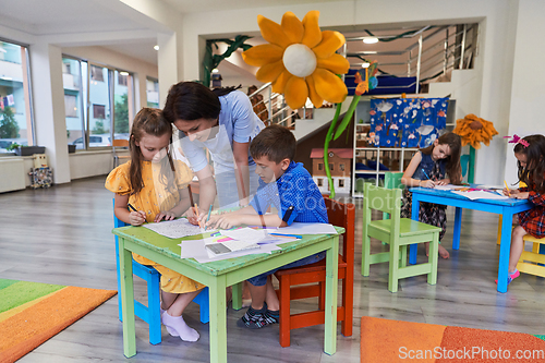 Image of Creative kids during an art class in a daycare center or elementary school classroom drawing with female teacher.