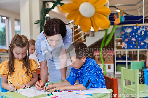 Image of Creative kids during an art class in a daycare center or elementary school classroom drawing with female teacher.