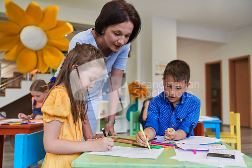 Image of Creative kids during an art class in a daycare center or elementary school classroom drawing with female teacher.