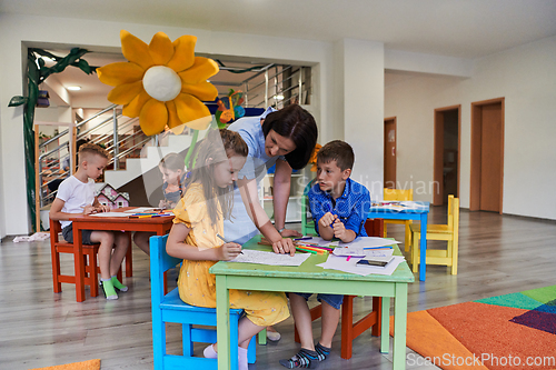 Image of Creative kids during an art class in a daycare center or elementary school classroom drawing with female teacher.