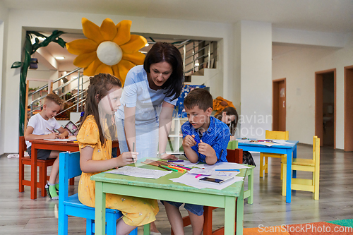 Image of Creative kids during an art class in a daycare center or elementary school classroom drawing with female teacher.