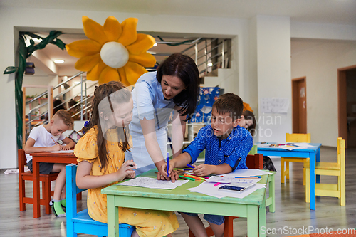 Image of Creative kids during an art class in a daycare center or elementary school classroom drawing with female teacher.