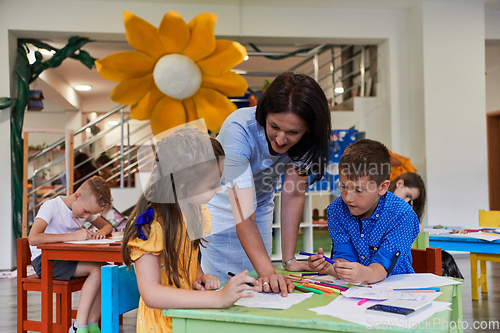 Image of Creative kids during an art class in a daycare center or elementary school classroom drawing with female teacher.