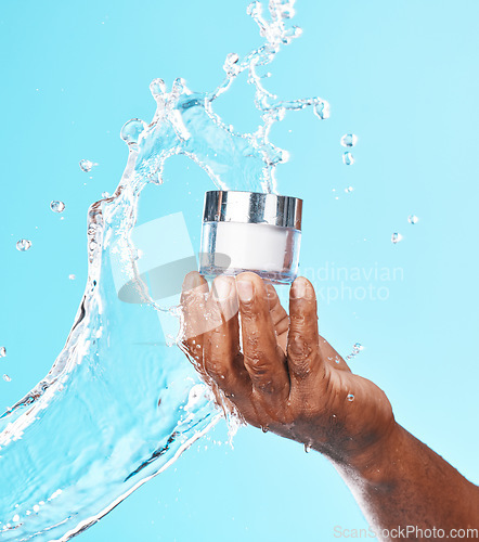 Image of Hand, water splash and black man with cream for skincare in studio on a blue background. Cosmetics, hygiene and male model holding lotion, creme or moisturizer product for healthy skin and beauty.