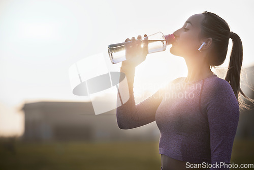 Image of Fitness, sunset and woman drinking water bottle after training workout, exercise and outdoor cardio running. Thirsty young athlete, sports hydration and nutrition for wellness, healthy body or energy