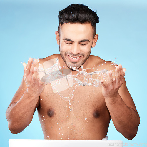 Image of Face, water splash and skincare of man cleaning in studio isolated on a blue background. Hygiene, water drops and male model washing, bathing or grooming for healthy skin, facial wellness or beauty.