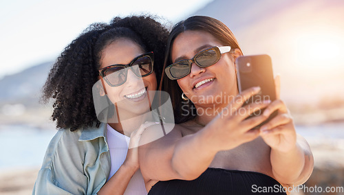 Image of Women, lgbtq and phone selfie at beach for love, travel and care on summer holiday, vacation or freedom. Sunglasses, lesbian and happy couple of friends taking mobile photograph, sea and social media