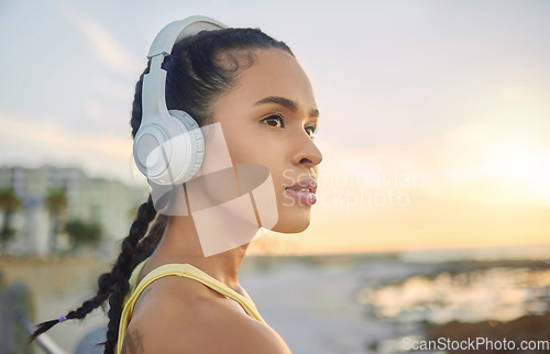 Image of Headphones, exercise music and woman at beach thinking about training, exercising or workout. Sports, fitness and female athlete streaming radio, podcast or audio after running at sunset by ocean.