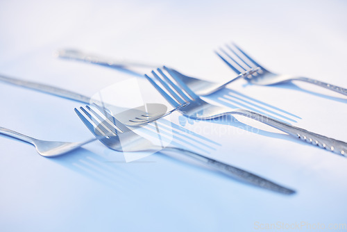 Image of Fork, cutlery and symmetry with eating utensils on a table in an empty studio on a blue background from above. Kitchen, utensil and forks closeup ready for breakfast, lunch or dinner in a restaurant