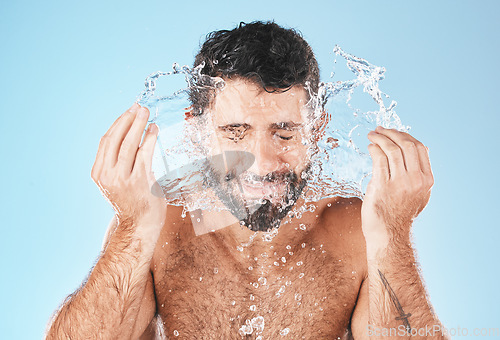 Image of Face, splash and man in studio for cleaning, wellness and personal health with self care by blue background. Model, facial and healthy with water splash, skincare and cosmetics by studio backdrop