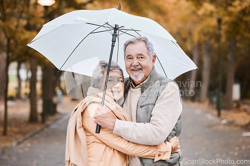 Image of Winter, hug and senior couple in a park, retirement date and walking in Canada with an umbrella. Nature affection, smile and portrait of an elderly man and woman on a walk for happiness and love