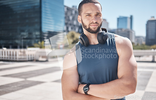 Image of Portrait, fitness and city with a sports man standing arms crossed while listening to music furing his workout. Exercise, health and wellness with a male athlete training outdoor in an urban town