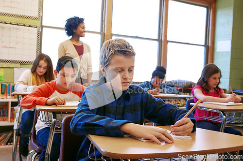 Image of Boy child, classroom and writing at desk, school and focus on education, development and learning for future. School kids, teacher and studying at table in class with diversity, notebook and pencil