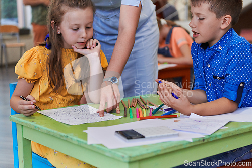 Image of Creative kids during an art class in a daycare center or elementary school classroom drawing with female teacher.