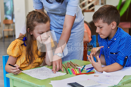 Image of Creative kids during an art class in a daycare center or elementary school classroom drawing with female teacher.