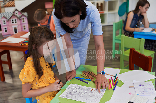 Image of Creative kids during an art class in a daycare center or elementary school classroom drawing with female teacher.