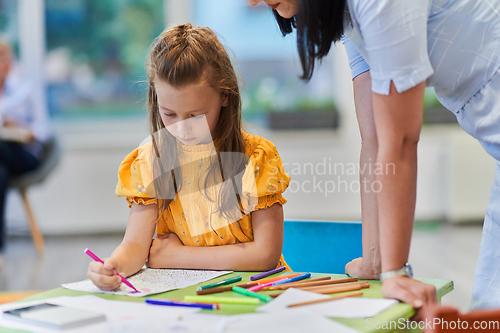 Image of Creative kids during an art class in a daycare center or elementary school classroom drawing with female teacher.