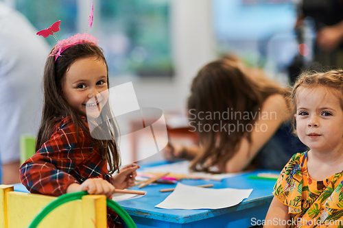 Image of Creative kids during an art class in a daycare center or elementary school classroom drawing with female teacher.