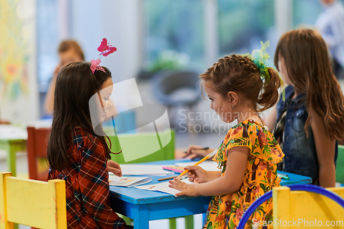 Image of Creative kids during an art class in a daycare center or elementary school classroom drawing with female teacher.