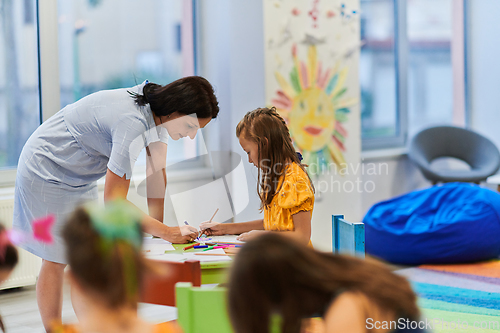 Image of Creative kids during an art class in a daycare center or elementary school classroom drawing with female teacher.